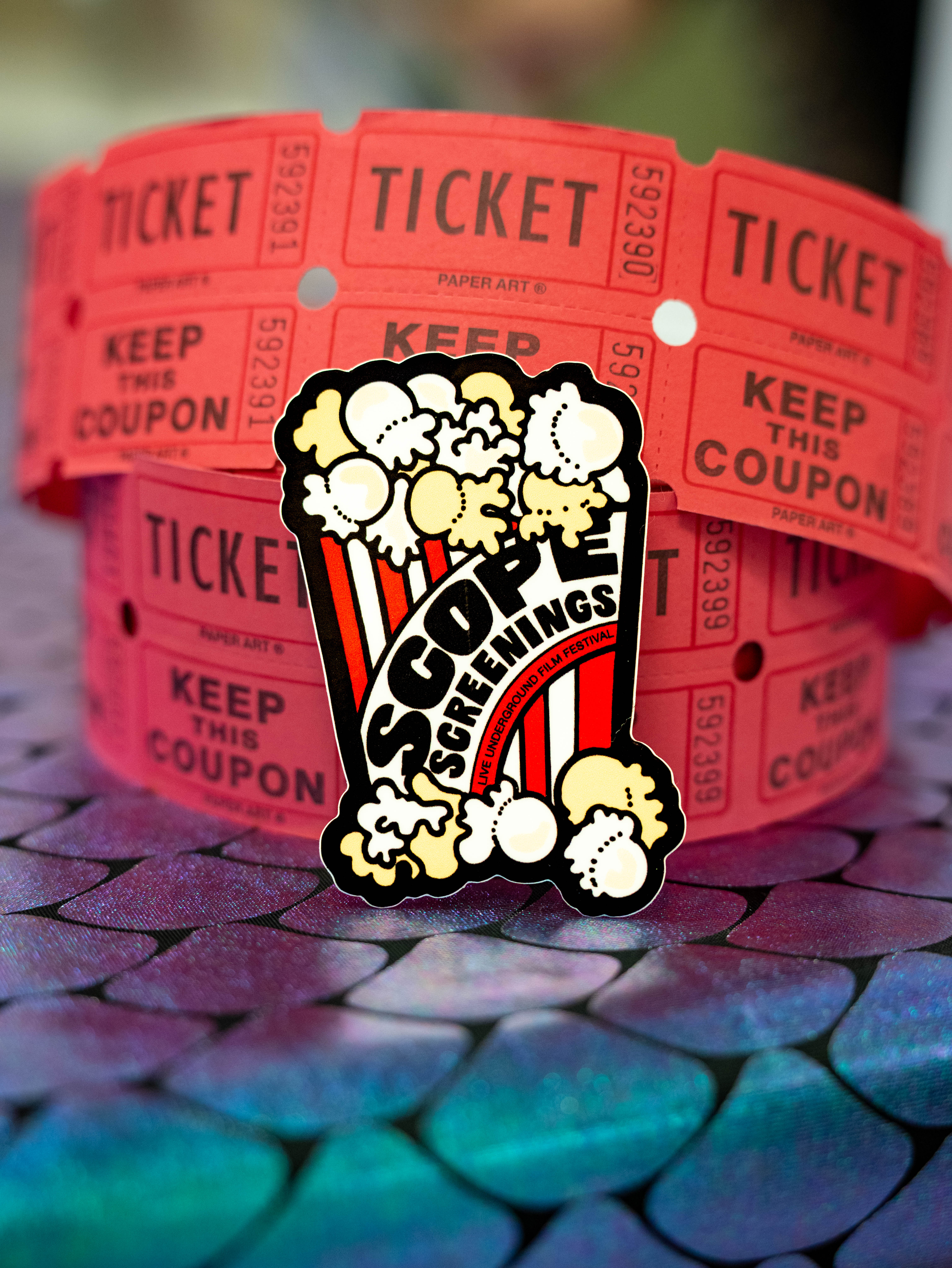Scope Screenings branded popcorn bucket with tickets — close-up product shot on teal mermaid-scale background